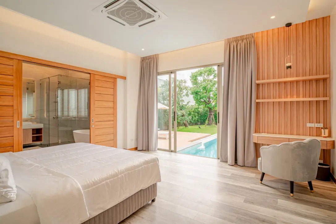 Modern hotel room with a king bed, wooden sliding doors to a glass-walled bathroom, and a view of a pool through large sliding doors on the patio.