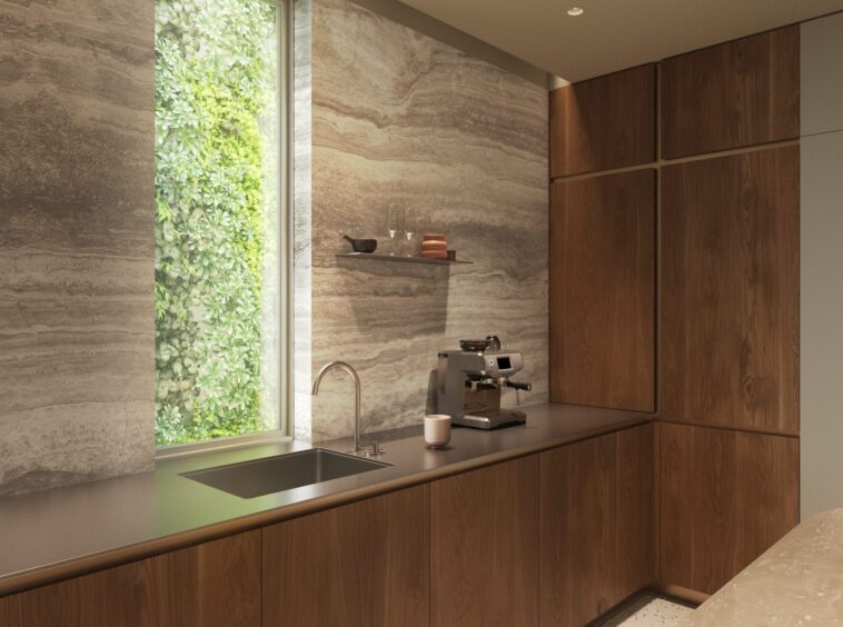 Modern kitchen with wood cabinets, gray countertop, and a vertical green plant wall beside a window; espresso machine and glassware on a shelf above the counter.