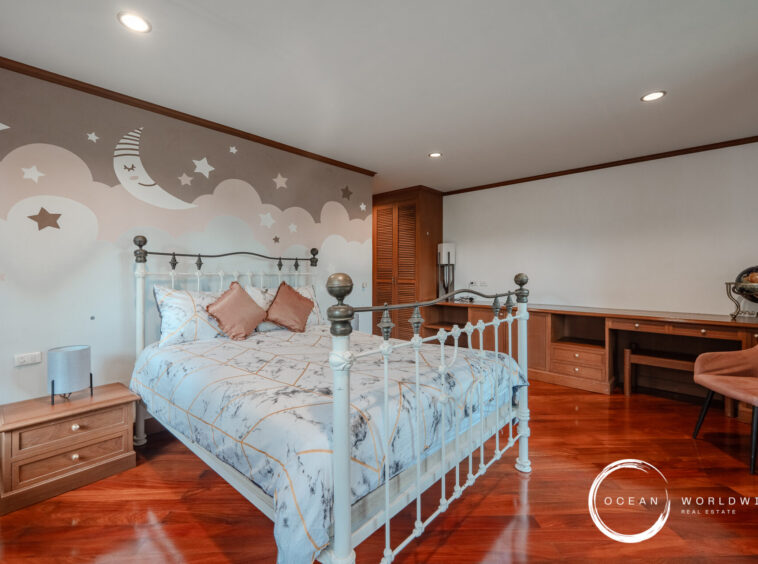 Bedroom with a pastel mural of moons and stars behind a white iron bed, marble-patterned bedding, wooden floor, and built-in desk area. Watermark reads 'Ocean Worldwide Real Estate' in the corner.