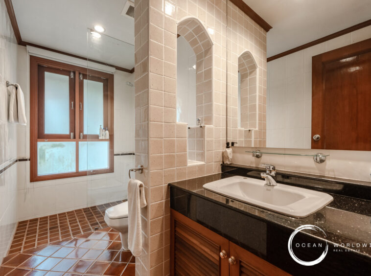 Bathroom with two sinks on a dark granite countertop and wooden cabinetry, separated by tiled arches