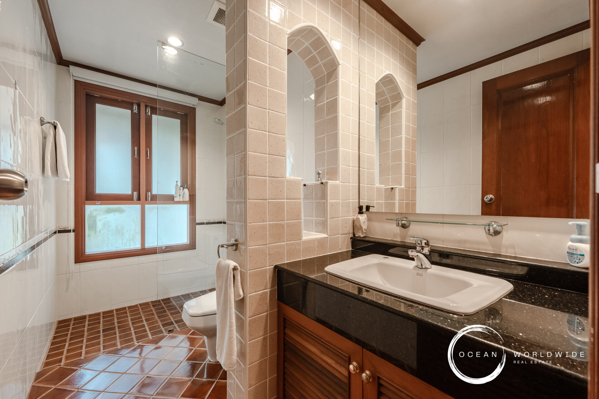 Bathroom with two sinks on a dark granite countertop and wooden cabinetry, separated by tiled arches