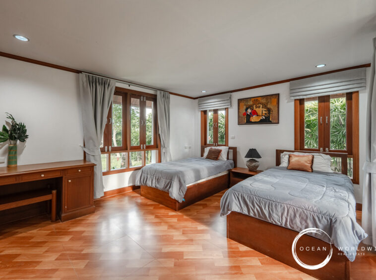 Twin beds in a bright wood-furnished bedroom with large windows, gray bedding, and a framed painting above the headboard.