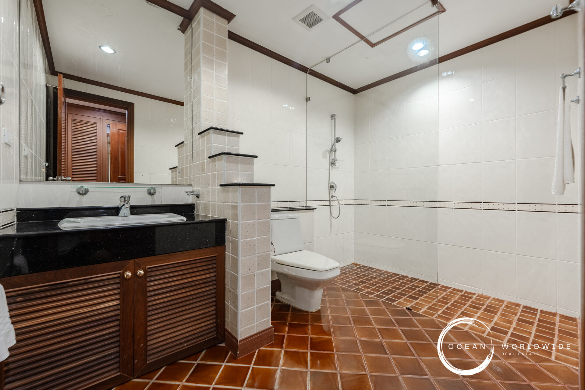 Bathroom with a wooden vanity, black countertop sink, large mirror, and glass shower enclosure.