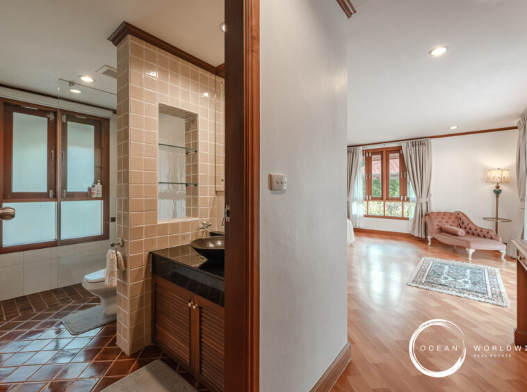 Bathroom with beige tiled walls and glass shower enclosure, next to a dark wood vanity and toilet, open to a living room view.