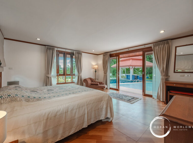 Hotel bedroom with a king bed, patterned cover, and beige curtains; sliding glass doors open to a pool area outside.