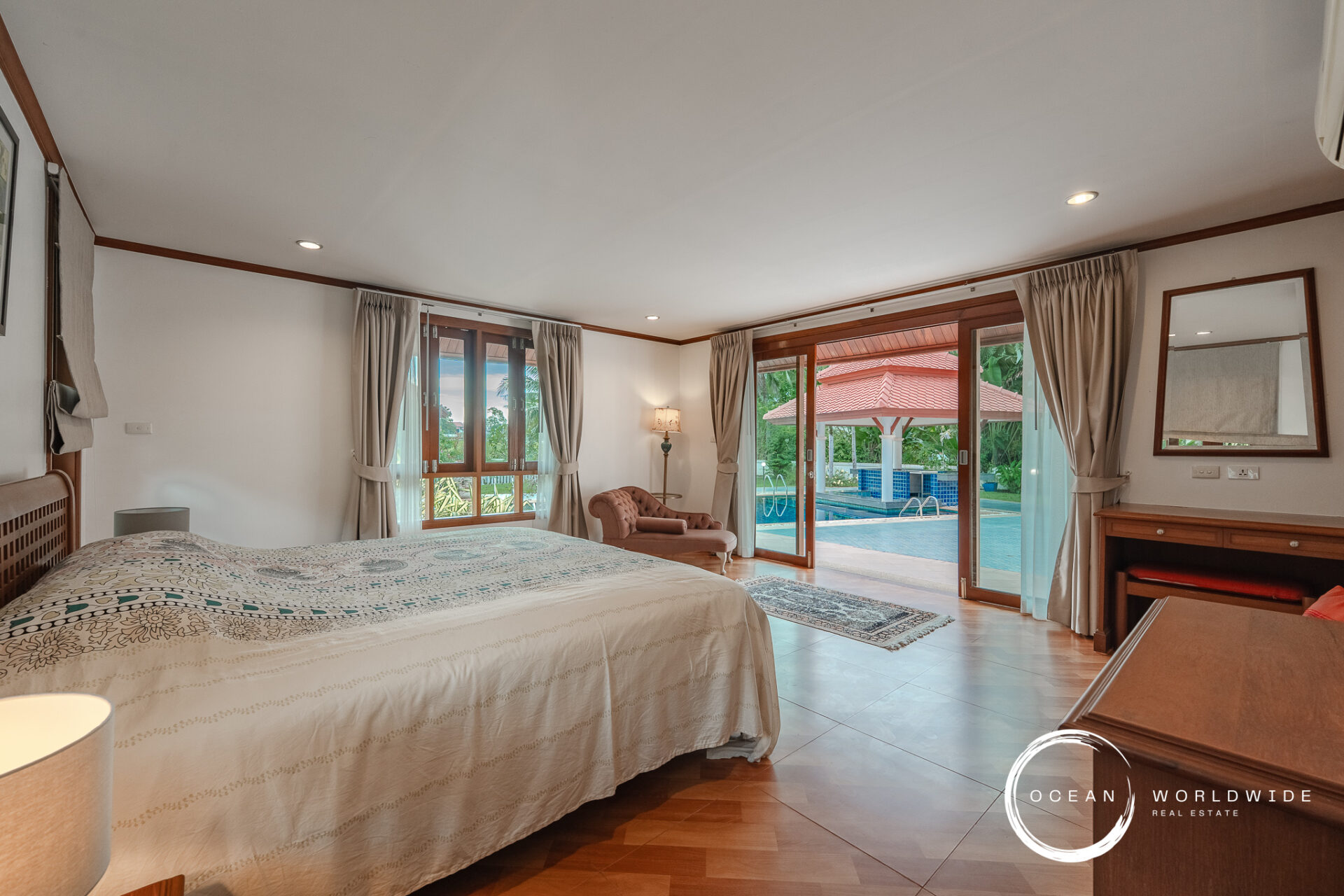 Hotel bedroom with a king bed, patterned cover, and beige curtains; sliding glass doors open to a pool area outside.