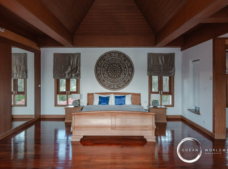 Bedroom with vaulted wooden beams, a large circular decorative wall piece above the wooden bed, and two matching nightstands with lamps on each side.