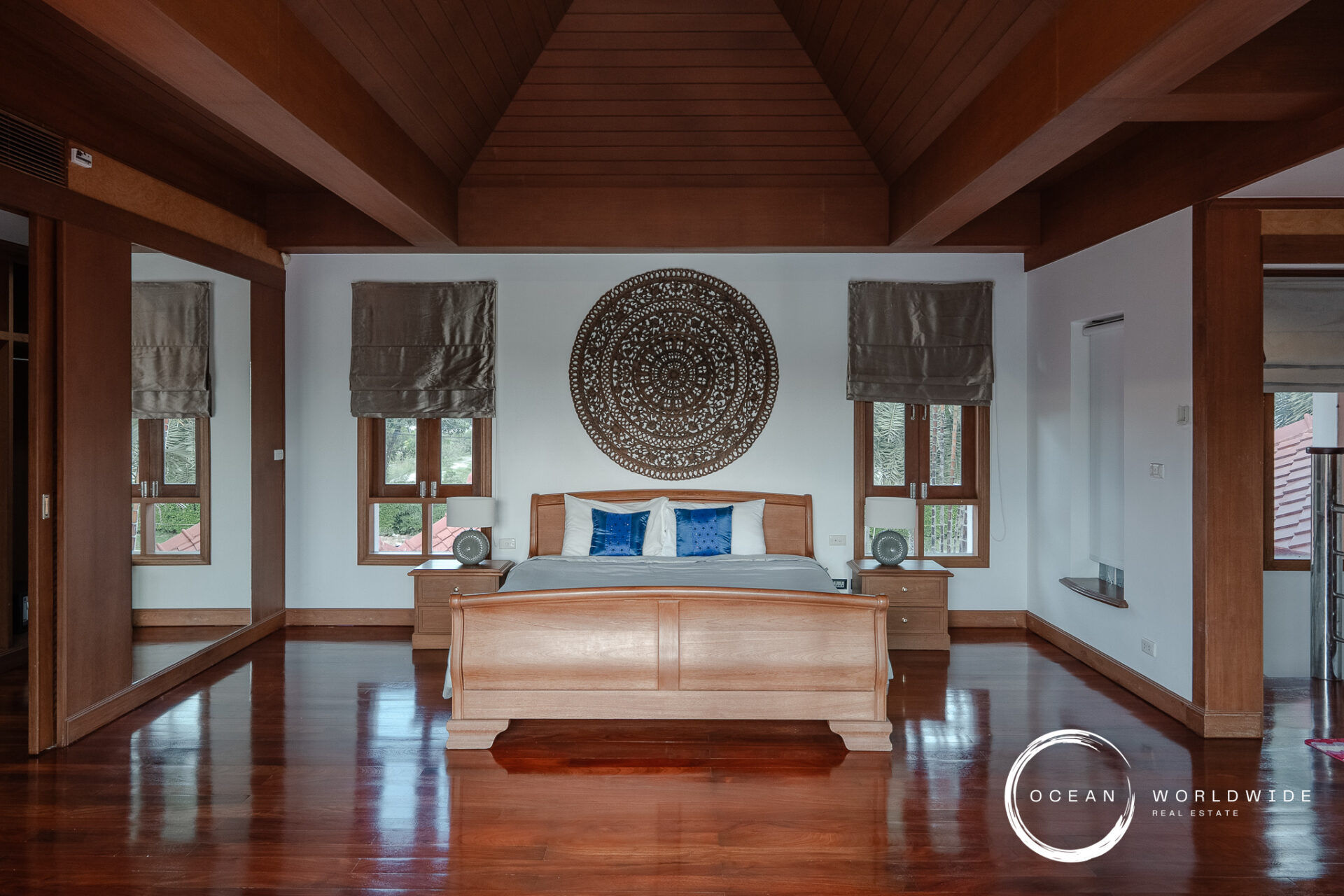 Bedroom with vaulted wooden beams, a large circular decorative wall piece above the wooden bed, and two matching nightstands with lamps on each side.
