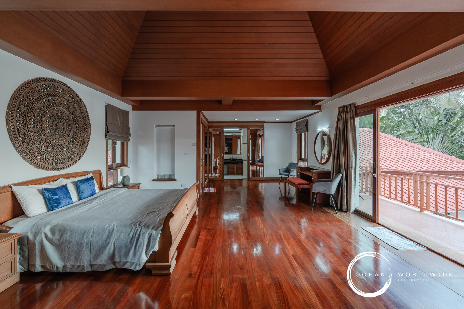 Luxurious bedroom with a wooden vaulted ceiling, king-size bed, blue pillows, and an ornate circular wall carving above the headboard.