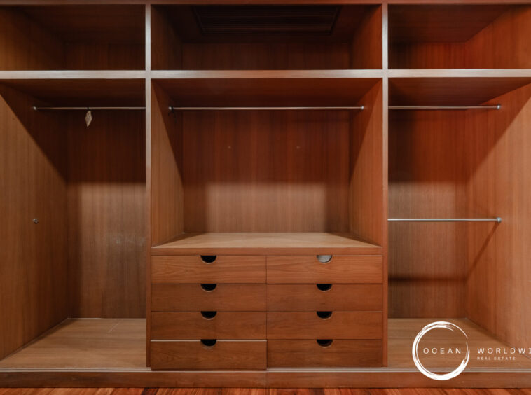 Wood built-in wardrobe with open compartments, two hanging rails, and central dresser drawers under a shelf row