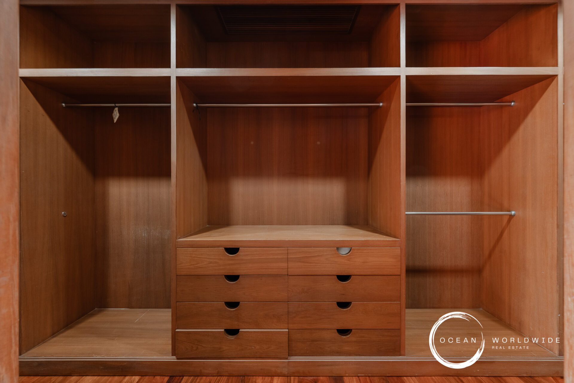Wood built-in wardrobe with open compartments, two hanging rails, and central dresser drawers under a shelf row