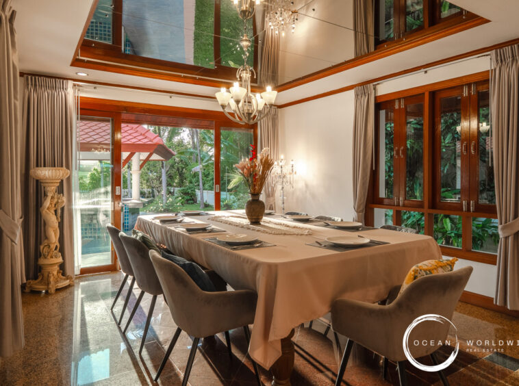 Elegant dining room with a long 表 table set for eight, beige tablecloths, gray upholstered chairs, and a crystal chandelier.