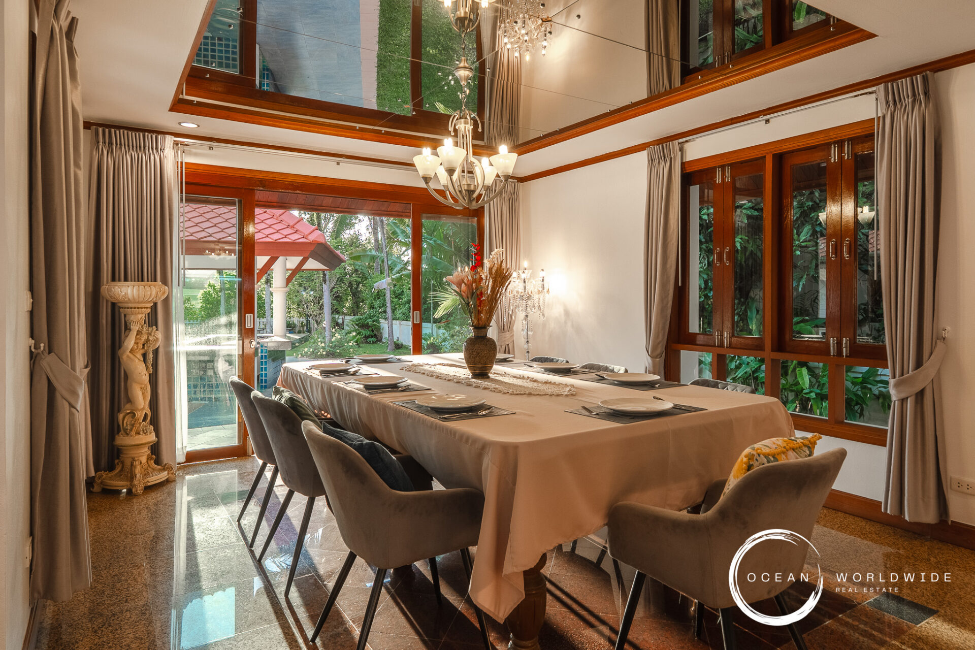 Elegant dining room with a long 表 table set for eight, beige tablecloths, gray upholstered chairs, and a crystal chandelier.