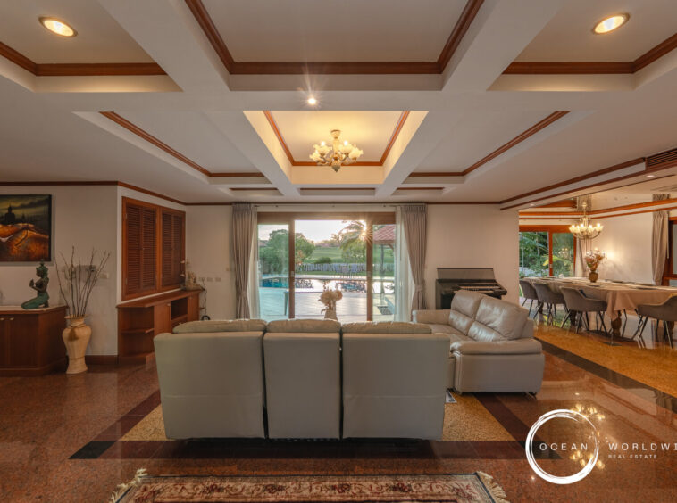 Spacious living area with a coffered ceiling, gray sectional sofa, and large glass doors facing a pool outside.