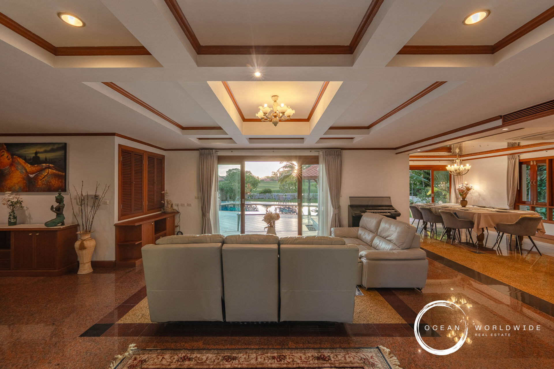 Spacious living area with a coffered ceiling, gray sectional sofa, and large glass doors facing a pool outside.