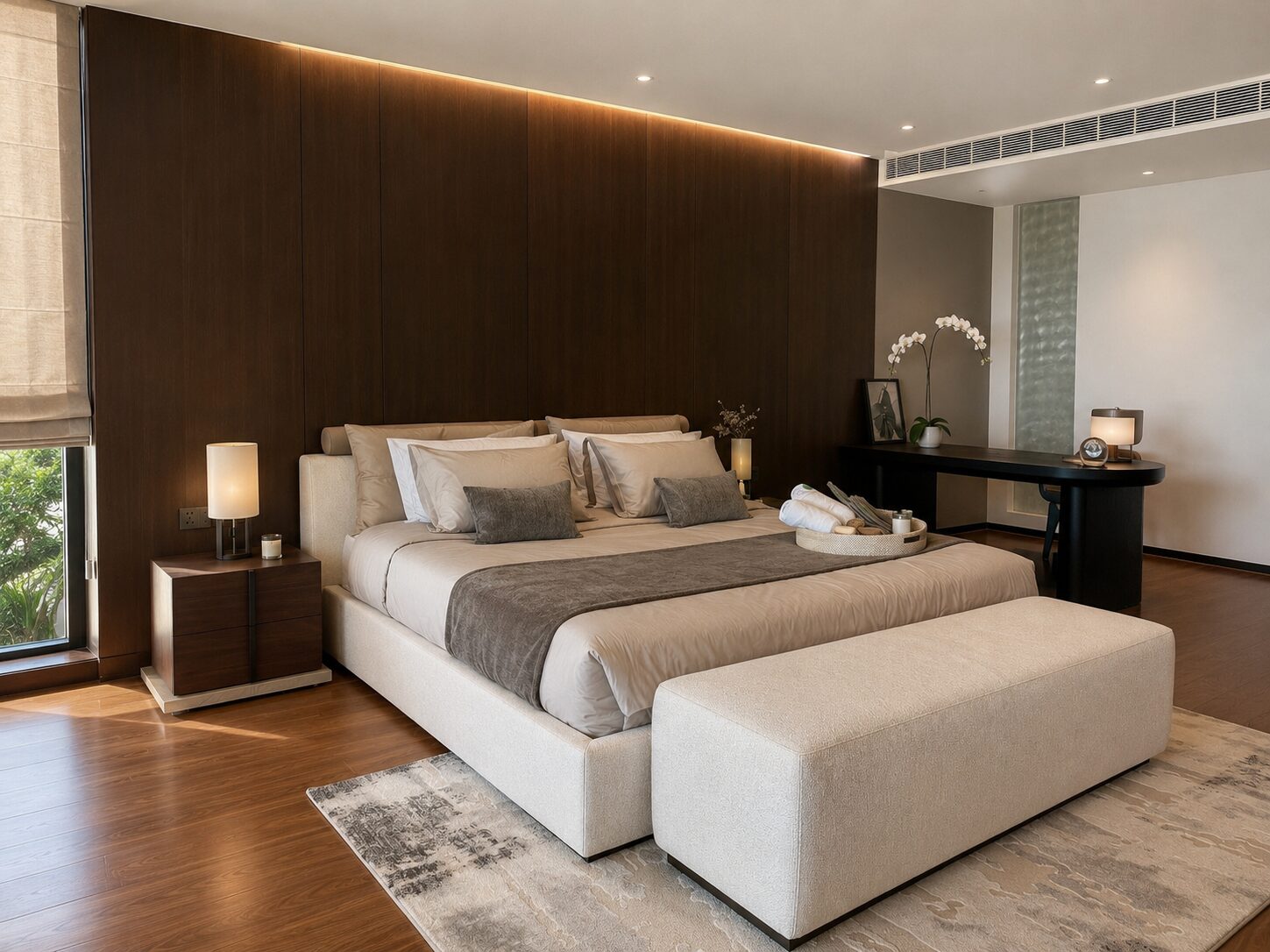 Master bedroom with beige upholstered bed, dark wood paneled wall, and a light gray ottoman at the foot of the bed.