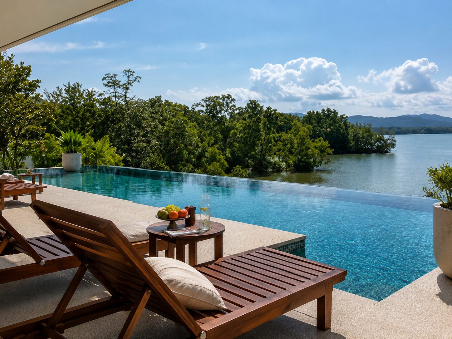 Infinity pool with wooden lounge chairs on a stone deck, overlooking a lake and green trees.