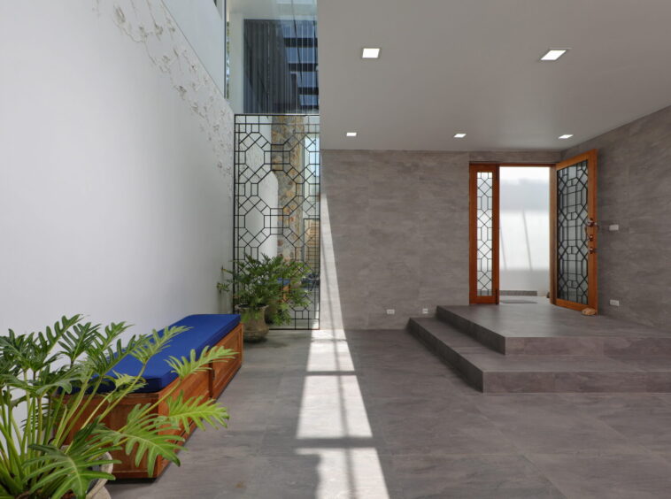 Modern interior entrance: grey tile floors and walls, steps to a wooden-framed door with geometric lattice glass, and potted plants along the left wall.