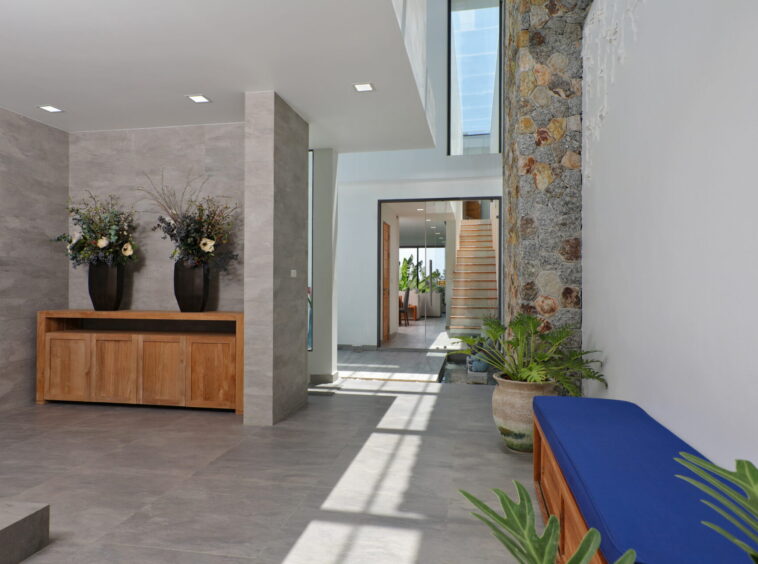 Modern lobby with gray tile walls, a wooden cabinet flanked by two black vases of flowers, and a stone wall on the right.