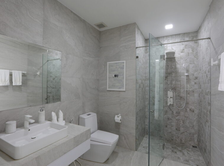 Gray marble bathroom with a wide rectangular sink, wall mirror, toilet, and a glass-enclosed shower area.