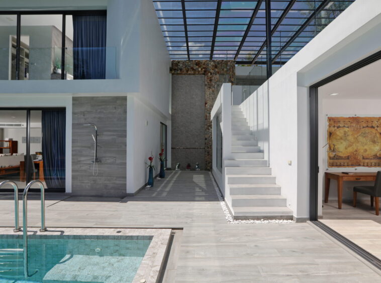 Open contemporary courtyard with a swimming pool, glass walls, white stairs, and a stone feature wall.
