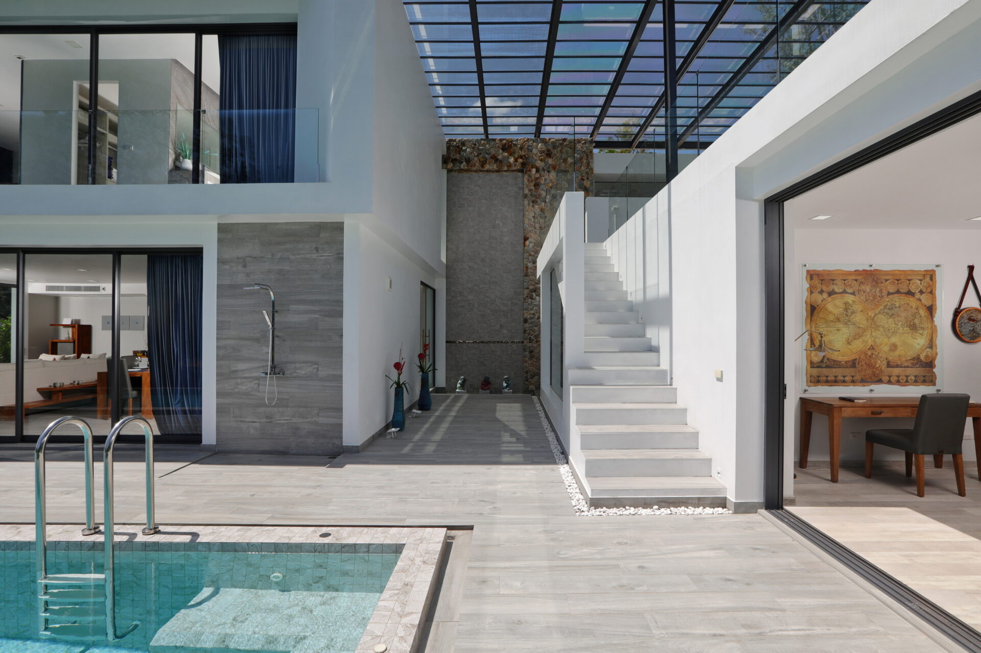 Open contemporary courtyard with a swimming pool, glass walls, white stairs, and a stone feature wall.