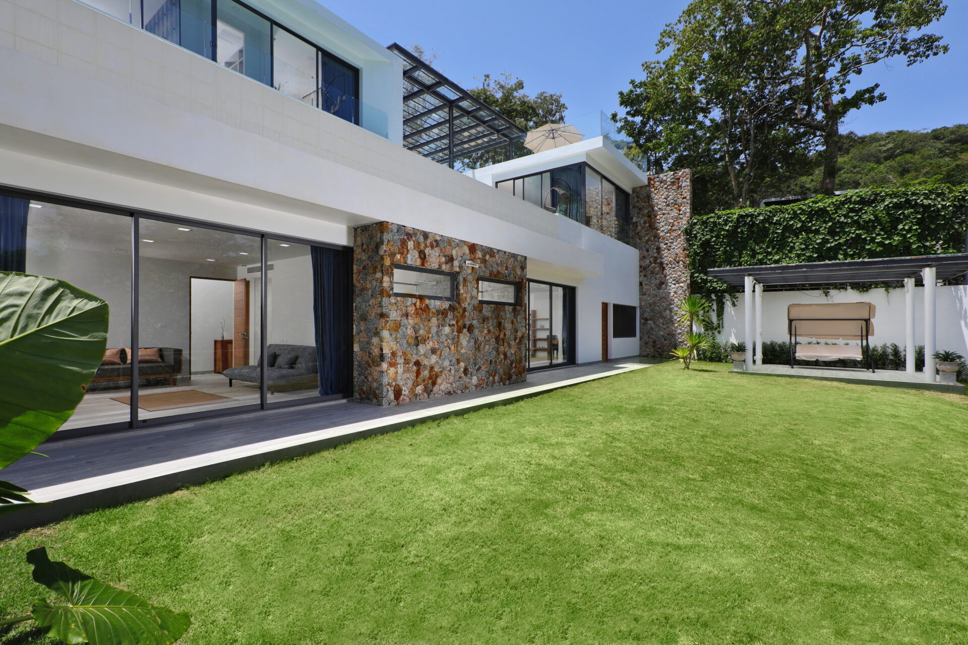 Modern house with glass walls and stone accents opening to a manicured lawn.
