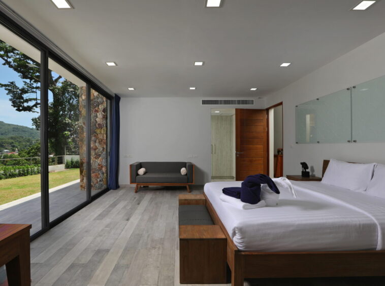 Hotel room with two white beds, wooden nightstands, and a large glass wall showing a green landscape outside.