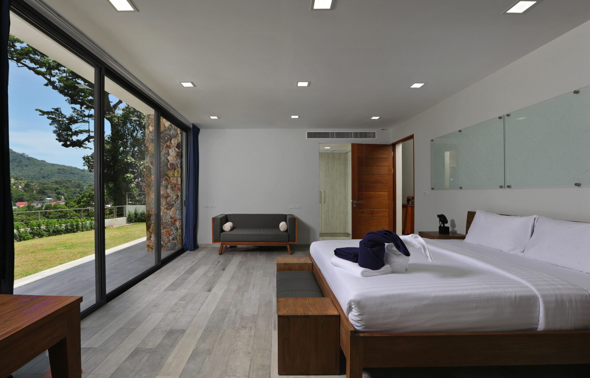 Hotel room with two white beds, wooden nightstands, and a large glass wall showing a green landscape outside.