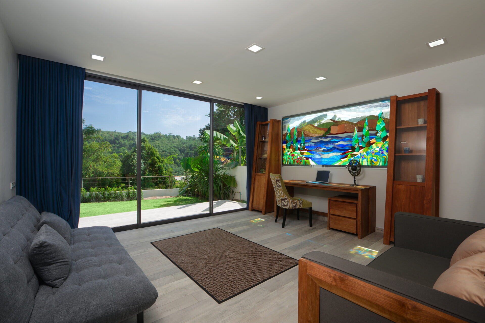 Living room with large glass sliding doors opening to a green lawn and trees, blue curtains frame the view.