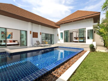 Modern villa with a blue tiled pool, glass sliding doors, and upward-sloped brown roofs; outdoor lounge area.