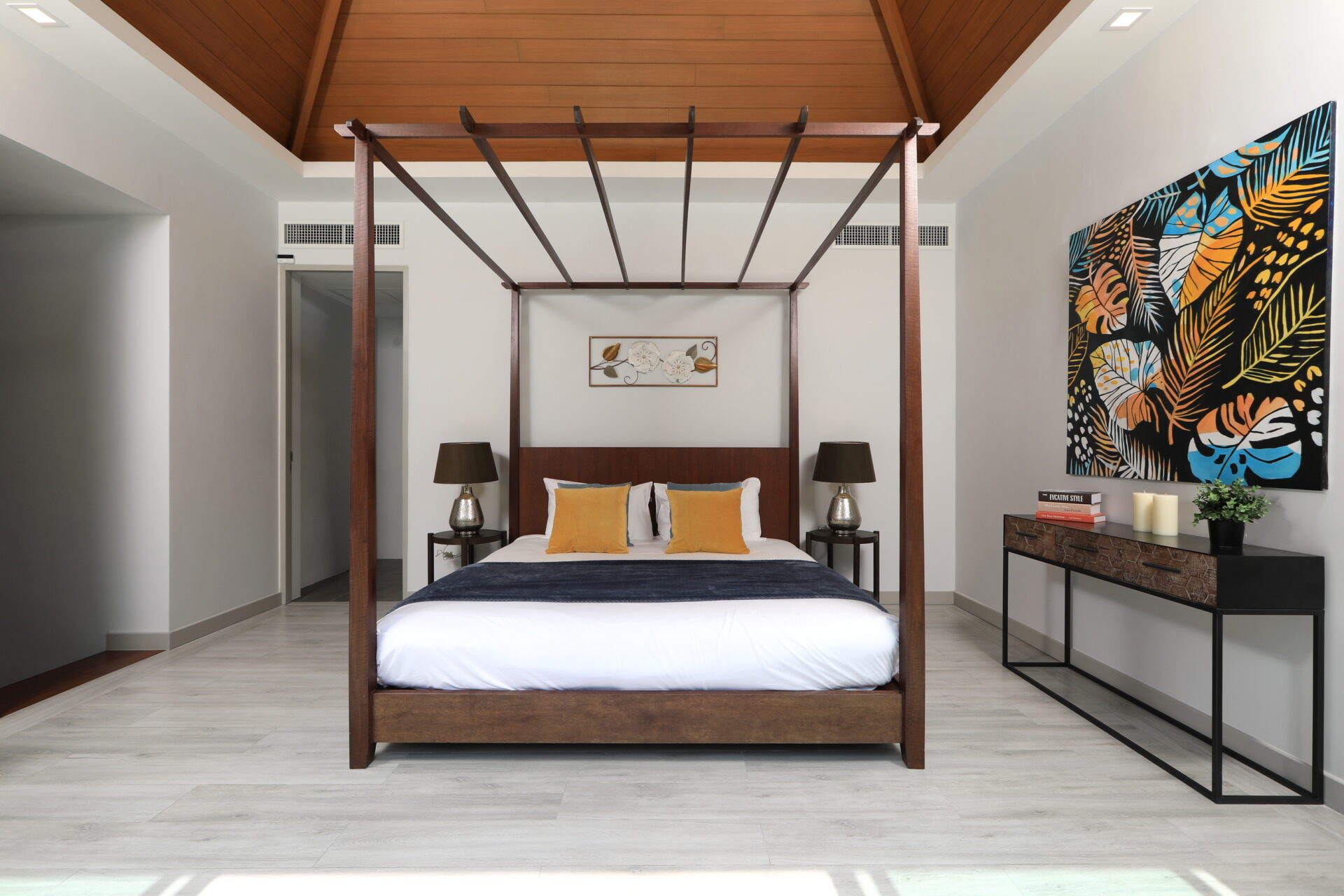 Modern bedroom with a dark wood four-poster bed, white bedding, and yellow accent pillows; brown lamps on each side.
