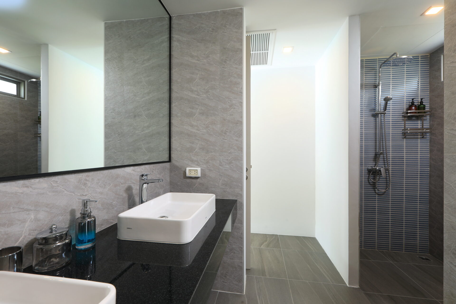 Modern bathroom with a double rectangular sink on a black countertop, large mirror, and a shower with blue tile wall nearby.