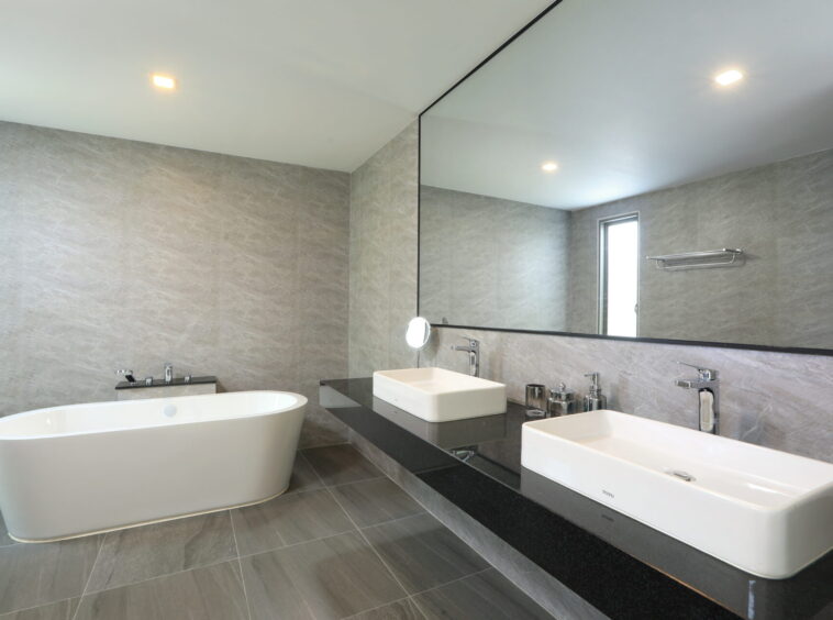 Modern bathroom with a white freestanding tub and dual square sinks on a black countertop beneath a large mirror. Used for a concierge-style bath room.