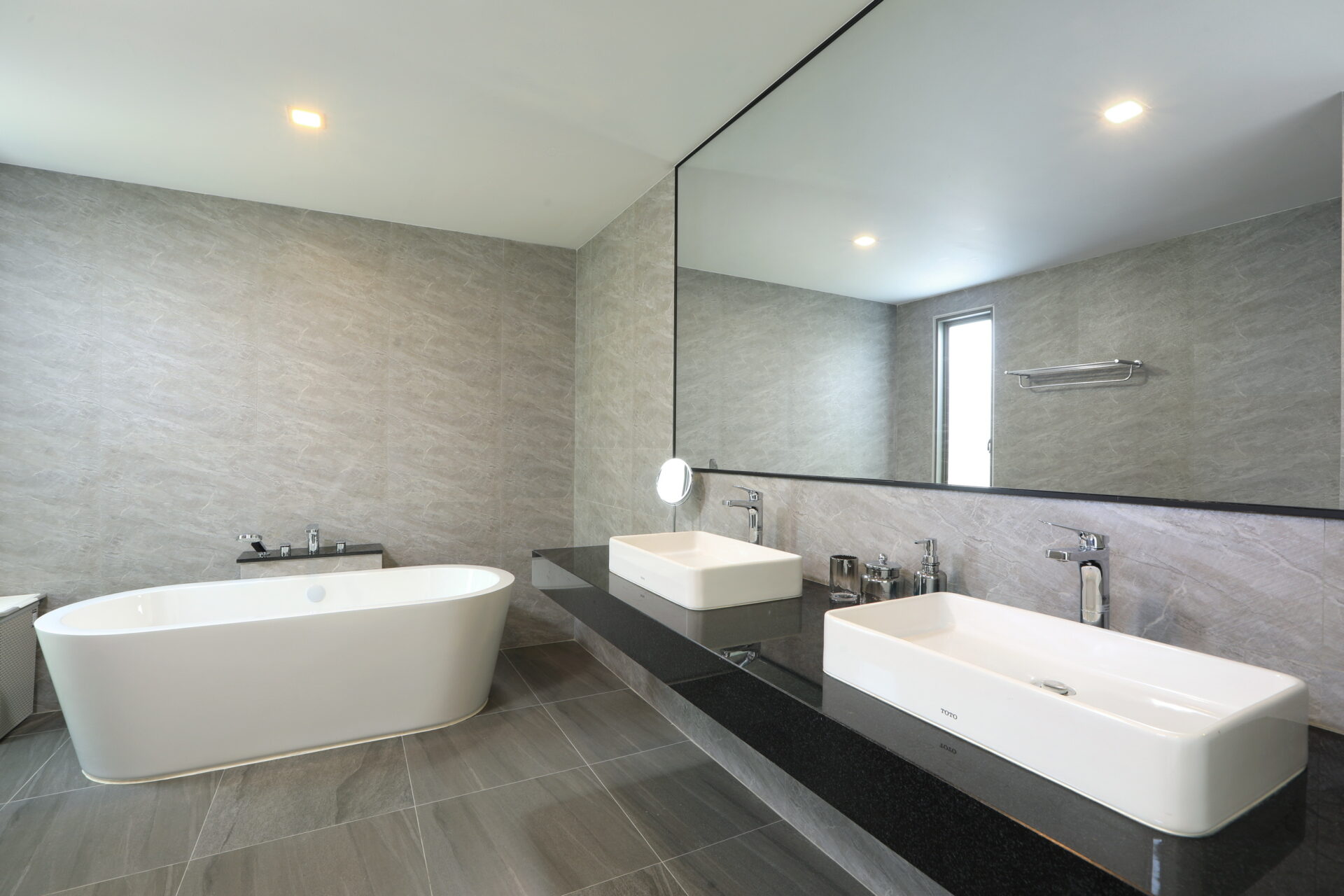 Modern bathroom with a white freestanding tub and dual square sinks on a black countertop beneath a large mirror. Used for a concierge-style bath room.