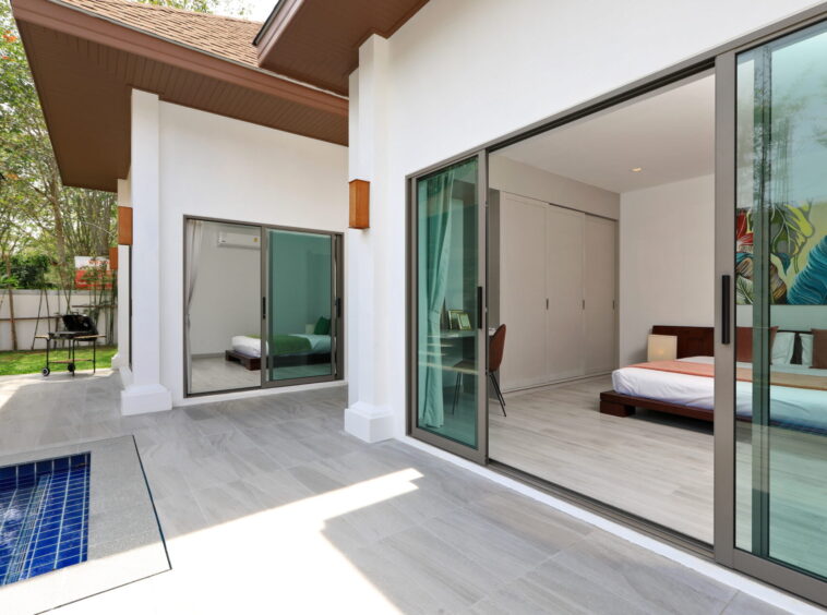 Patio with light gray tiles, pool nearby, and large glass doors opening to a sunlit bedroom.