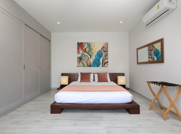 Modern bedroom with a low wooden platform bed, white bedding, peach throw, and two matching lamps on dark nightstands.