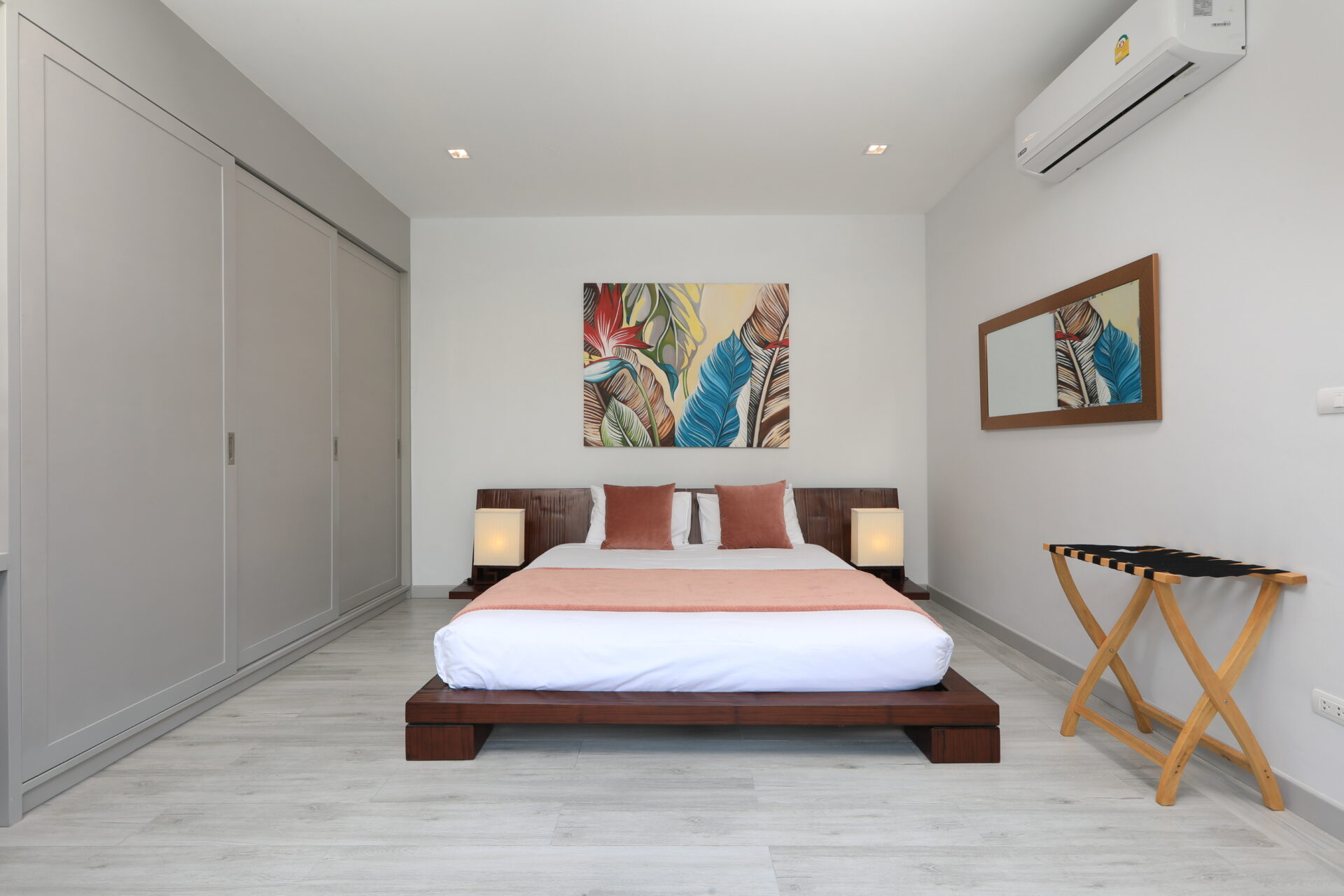 Modern bedroom with a low wooden platform bed, white bedding, peach throw, and two matching lamps on dark nightstands.