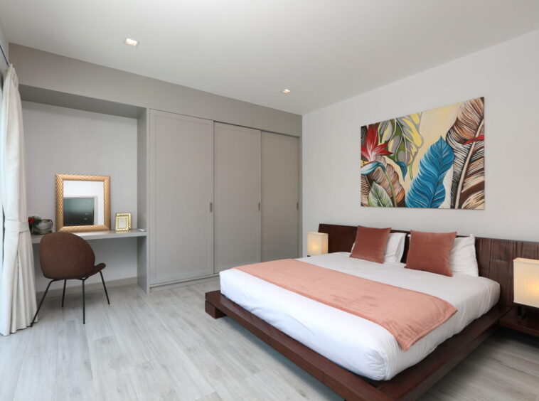 Modern bedroom with a low wooden bed, pink accents, and a colorful tropical leaf artwork above the headboard