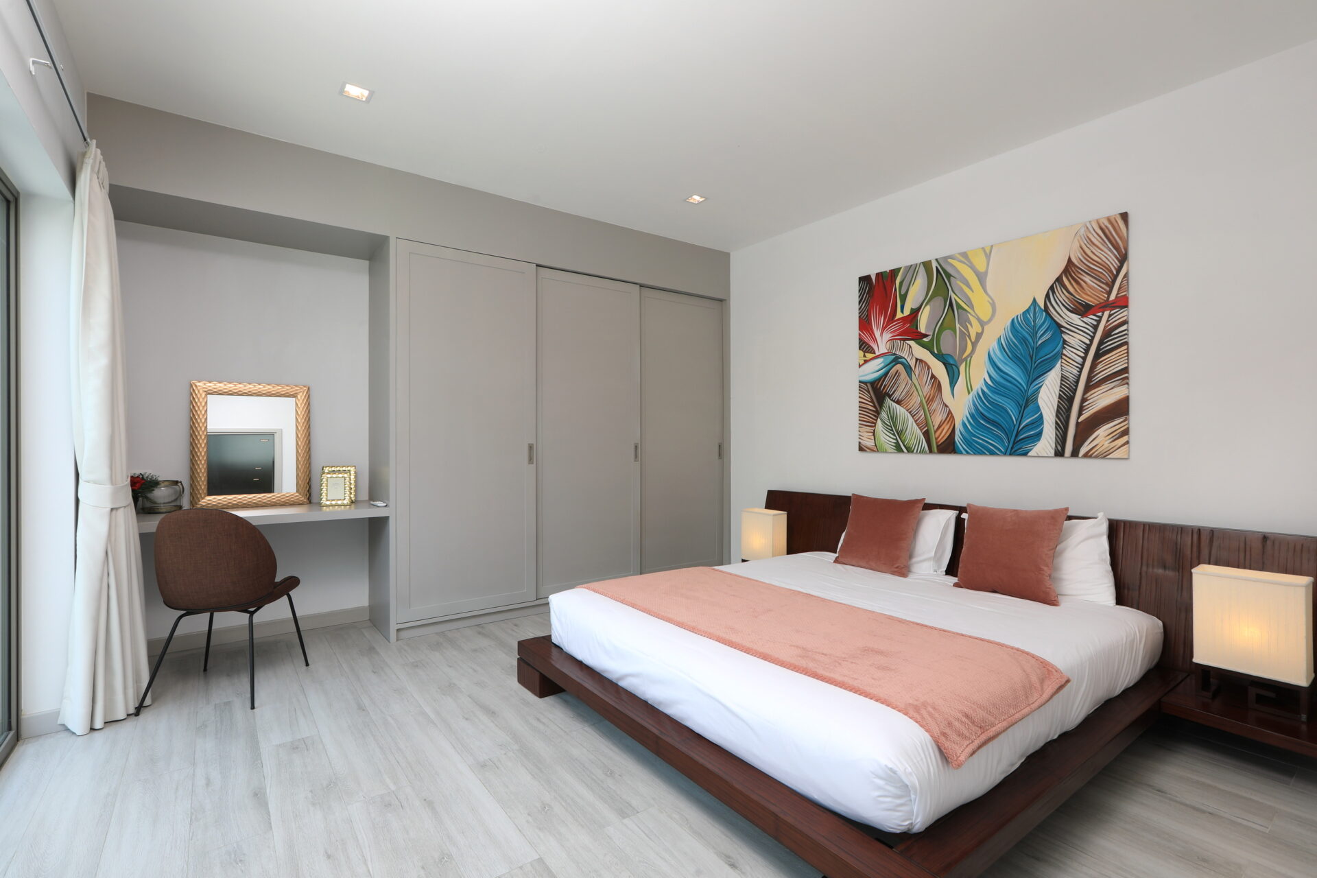 Modern bedroom with a low wooden bed, pink accents, and a colorful tropical leaf artwork above the headboard