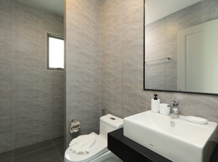 Modern bathroom with gray marble walls, a white rectangular sink on a black countertop, and a large framed mirror above it.