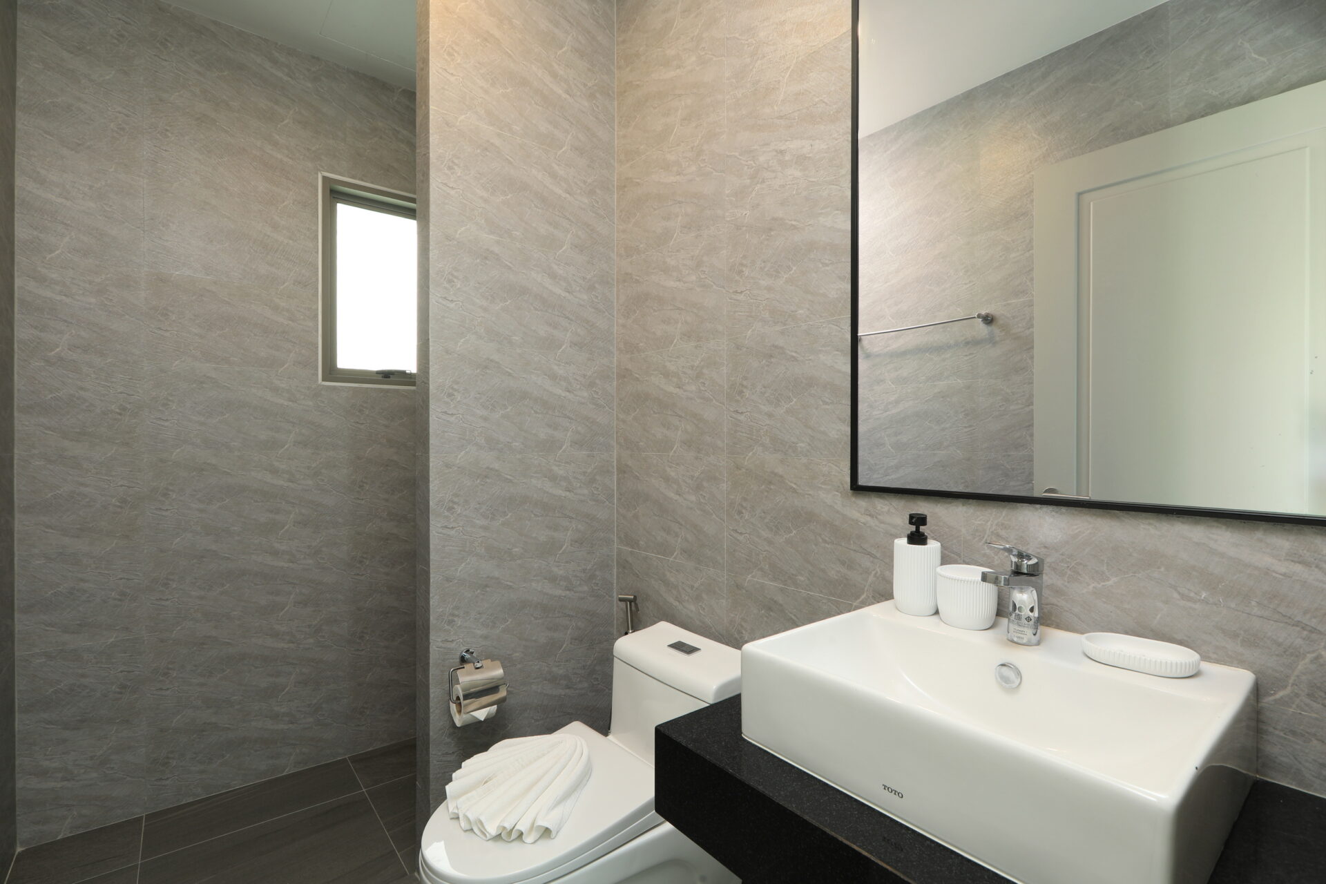 Modern bathroom with gray marble walls, a white rectangular sink on a black countertop, and a large framed mirror above it.