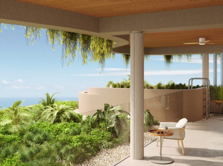 Open-air patio with tropical plants, beige curved walls, and an ocean view beyond a glass railing.