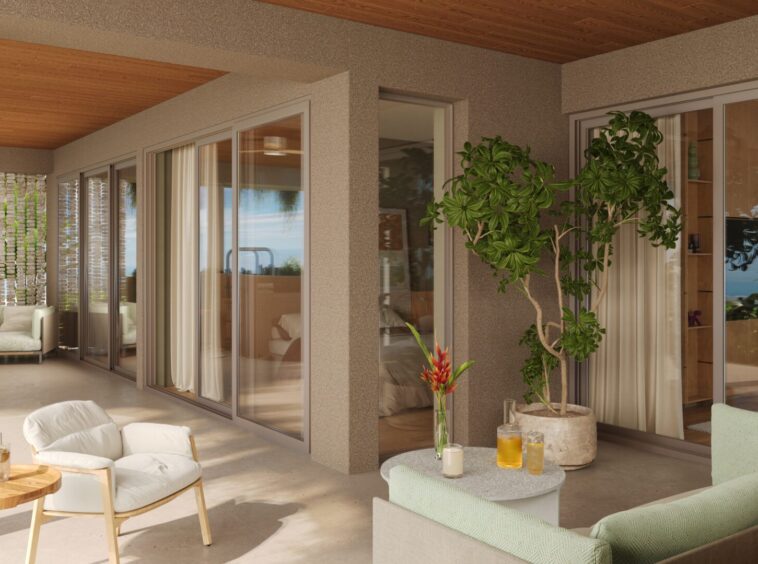 Sunlit covered patio with white cushioned seating, round wooden table, and potted plants, ocean view in the distance.