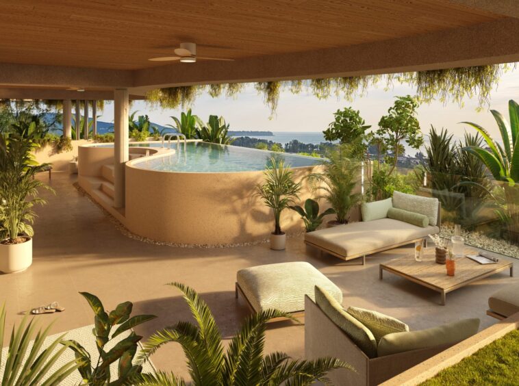 Sunlit outdoor lounge with a curved infinity pool, beige seating, and lush tropical plants overlooking the coastline and distant hills.