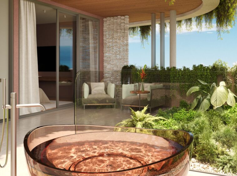 Circular copper hot tub on a sunlit patio with glass railing and lush greenery, overlooking the ocean.