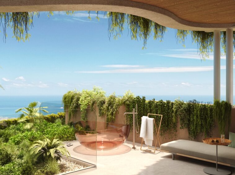 Modern outdoor lounge on a terrace with lush plants, glass railing, and a view of the ocean under a clear blue sky.