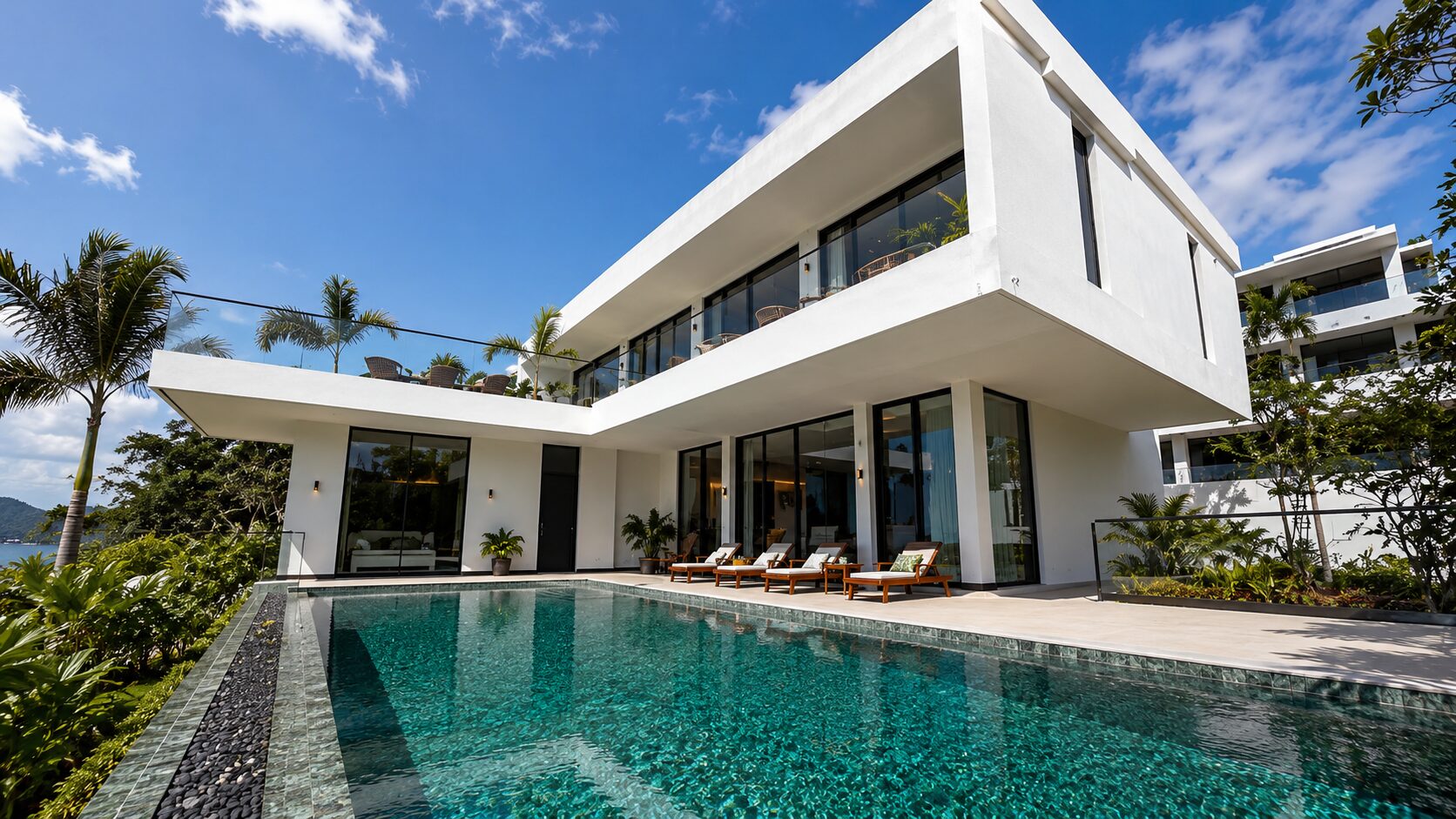Modern white villa with glass walls, a rectangular pool, and palm trees under a bright blue sky; outdoor lounge chairs line the pool deck.