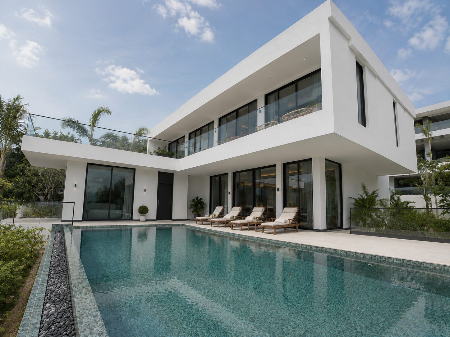 Modern white two‑story villa with glass balcony and a rectangular pool in the foreground to the left.