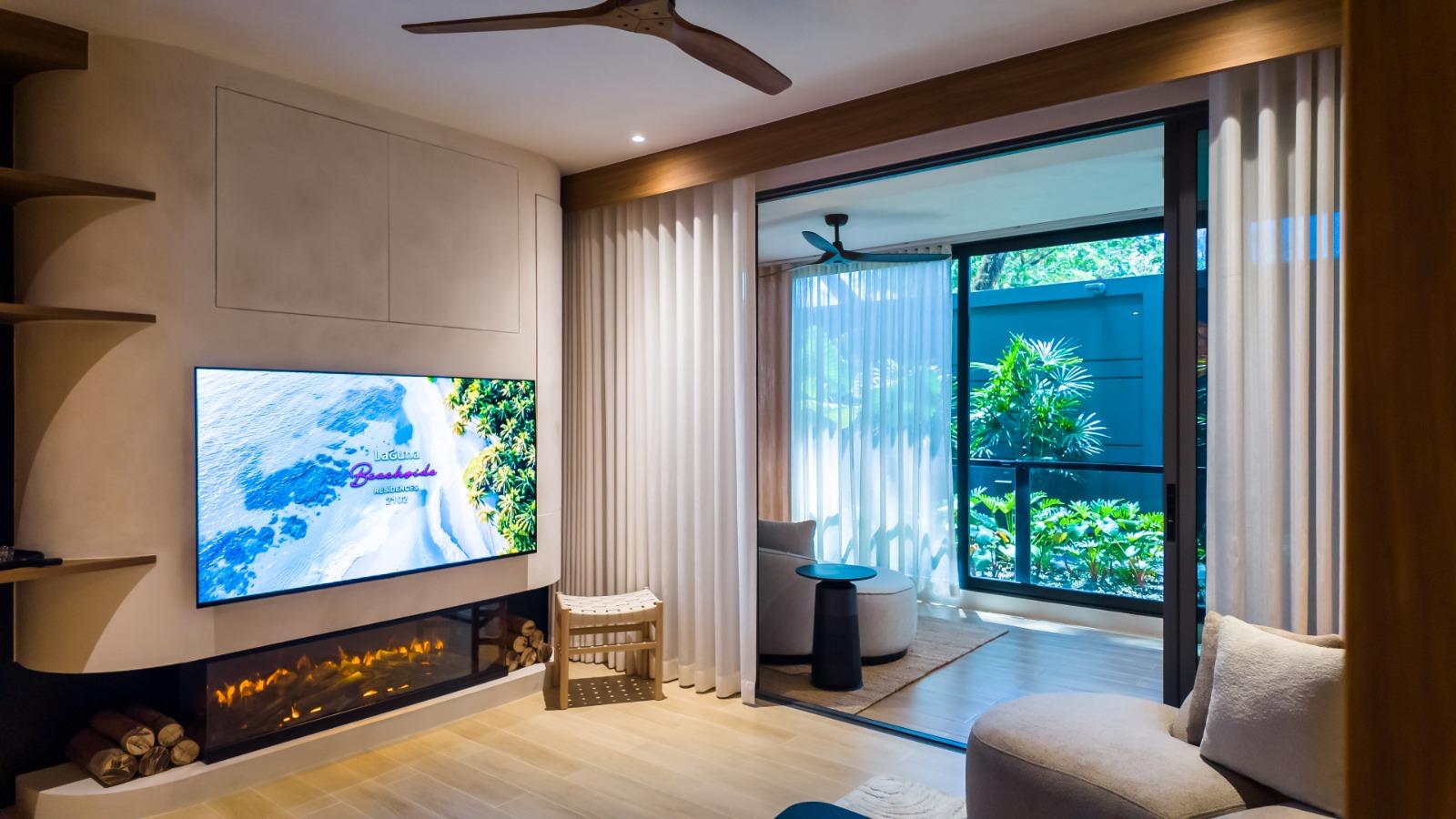 Modern living room with a wall-mounted flat-screen TV above a linear gas fireplace, cream-curtain-clad windows, and exposed wooden details.